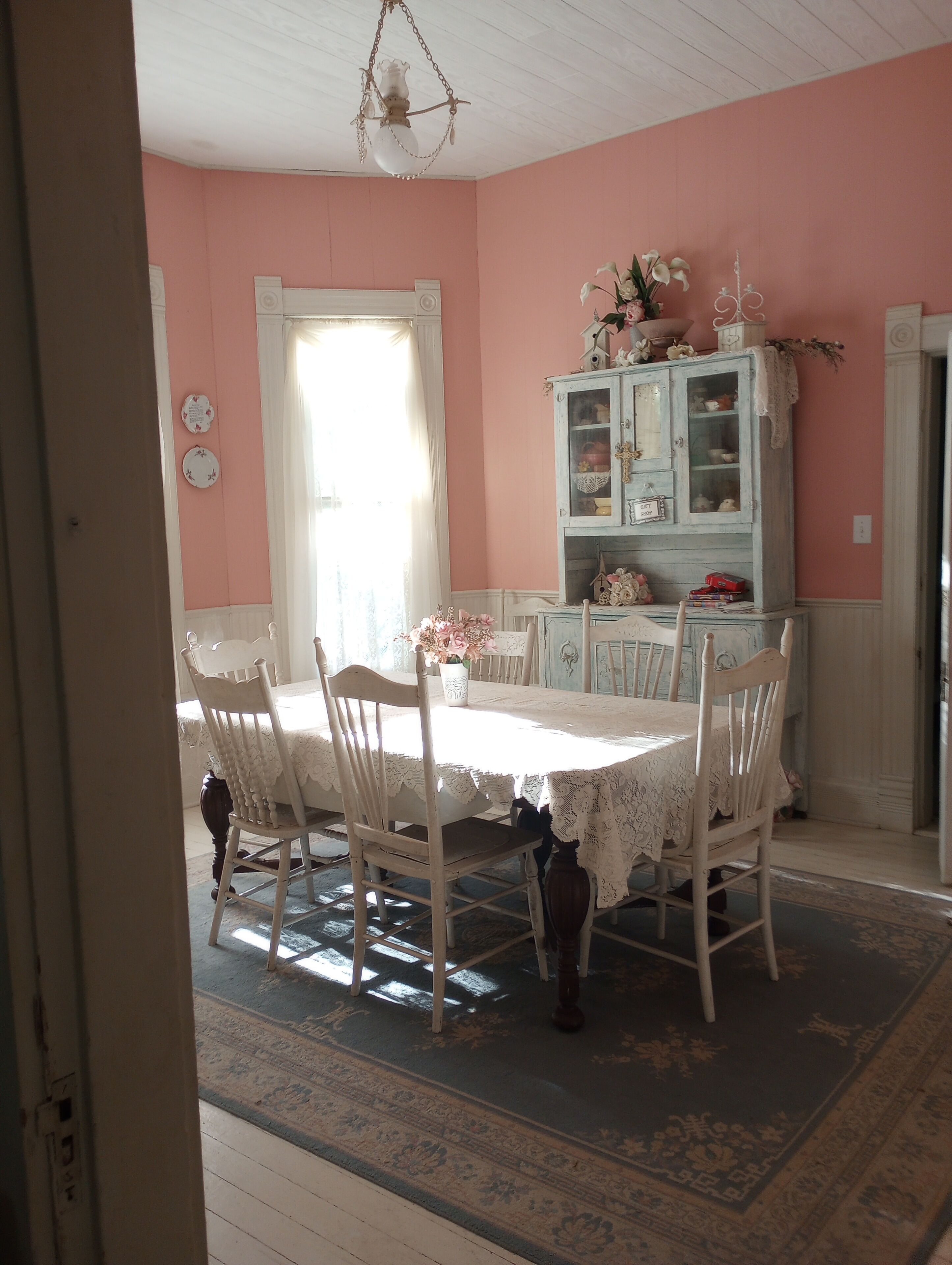 A dining area with a table set for four, surrounded by white chairs, a blue cabinet with glass doors, and a floral arrangement on the table.