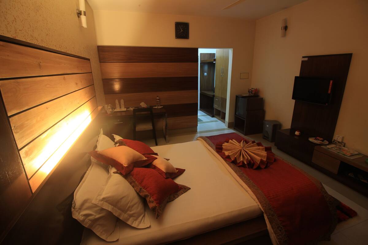 Une chambre d’hôtel avec une tête de lit en bois, un lit avec une literie rouge et blanche, un bureau avec une chaise, une télévision et une armoire.