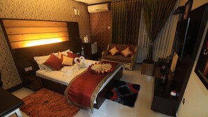 A hotel room with a large bed, a sofa, a TV, and a desk.
