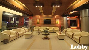 A lobby with a modern design, featuring leather sofas arranged in a U-shape, a central coffee table, and a flat-screen TV mounted on the wall.