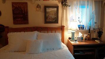 A neatly made bed with a patterned bedspread, a wooden headboard, and a bedside table with a lamp, a bottle, and a small figurine.