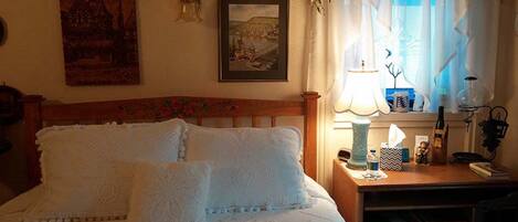A neatly made bed with a patterned bedspread, a wooden headboard, and a bedside table with a lamp, a bottle, and a small figurine.
