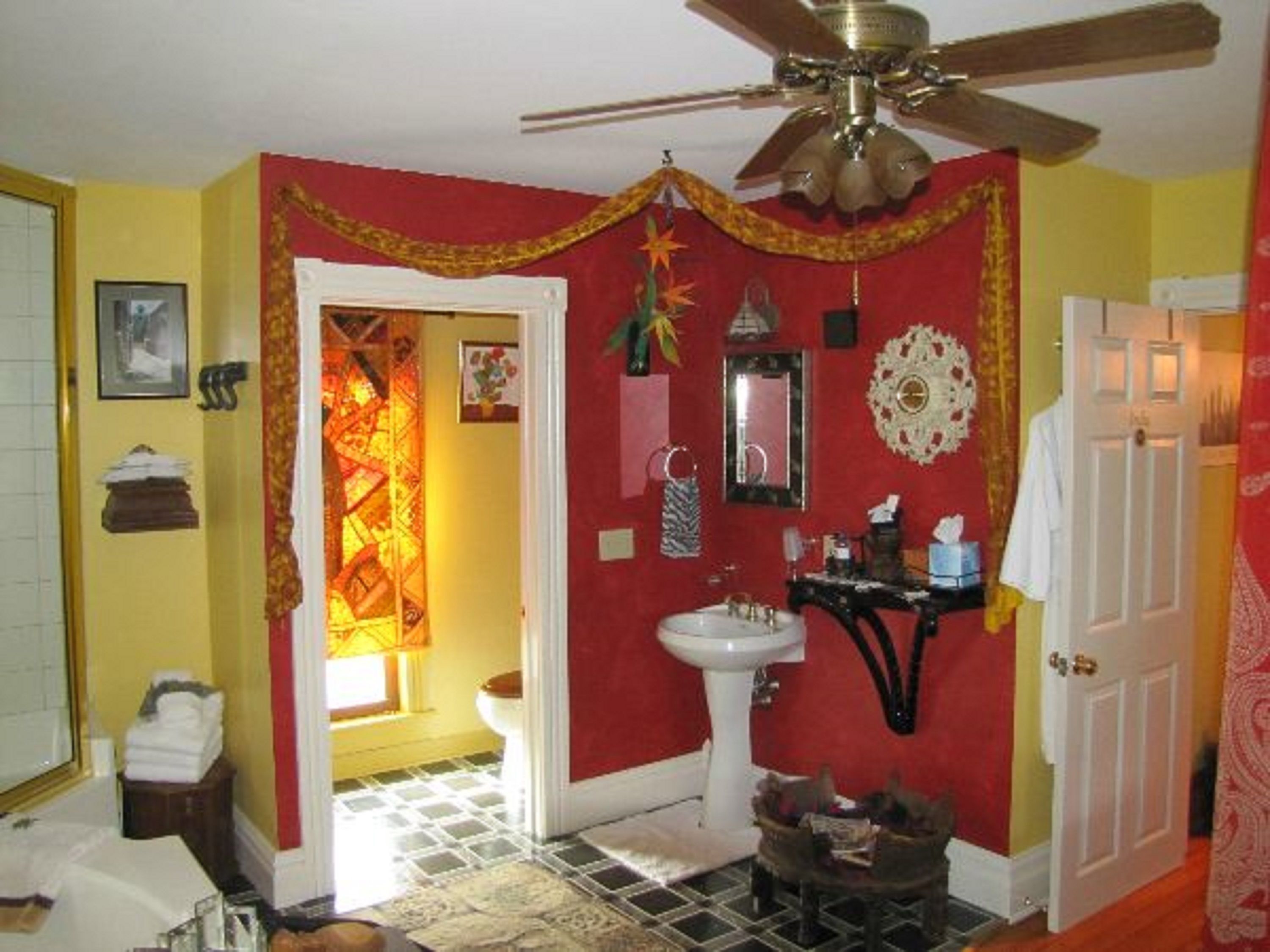 A bathroom with a red accent wall, a white sink, a ceiling fan, and a tiled floor.