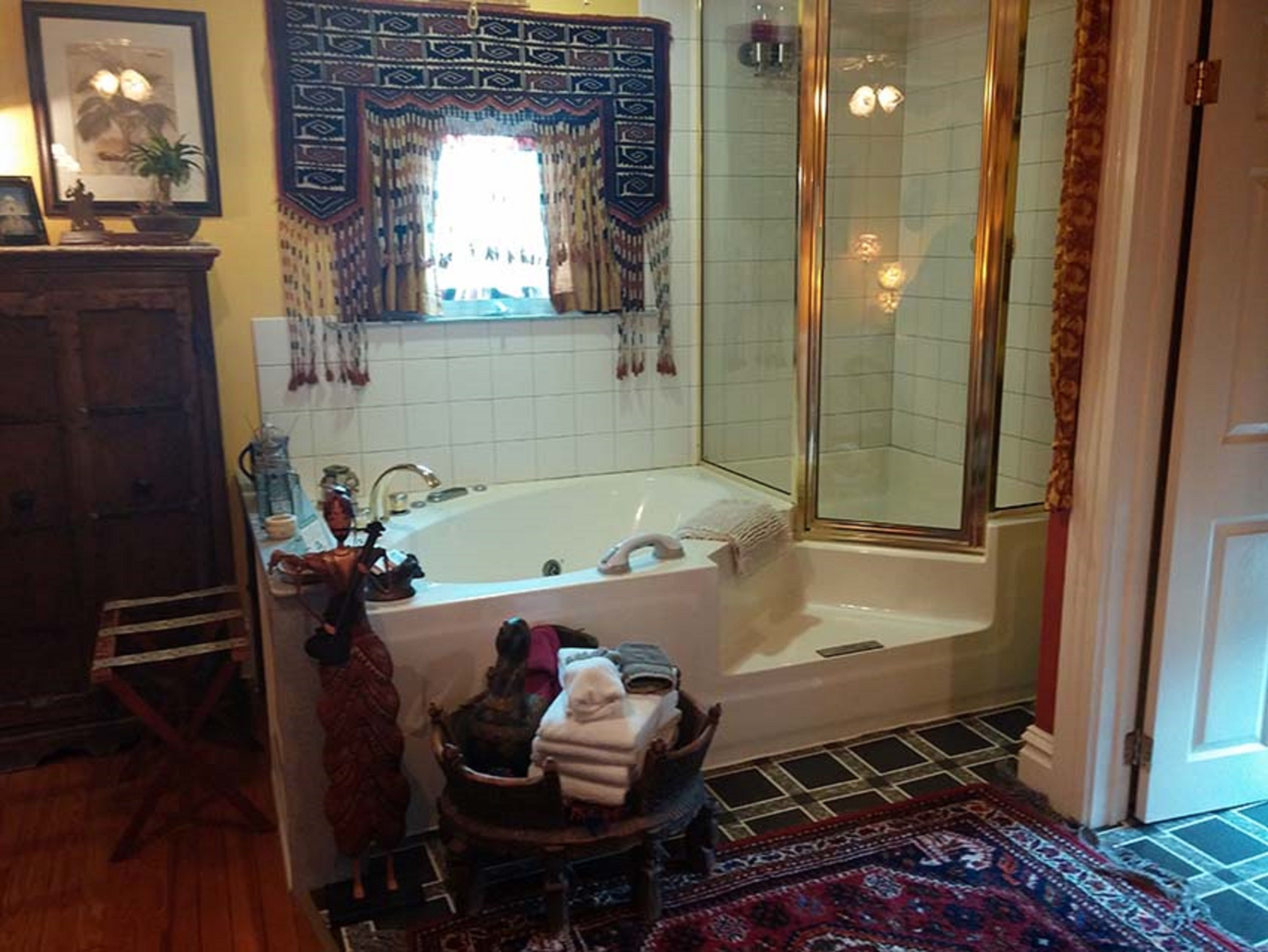 Une salle de bain avec une baignoire, une douche et un lavabo. Il y a un tapis sur le sol et une chaise en bois.