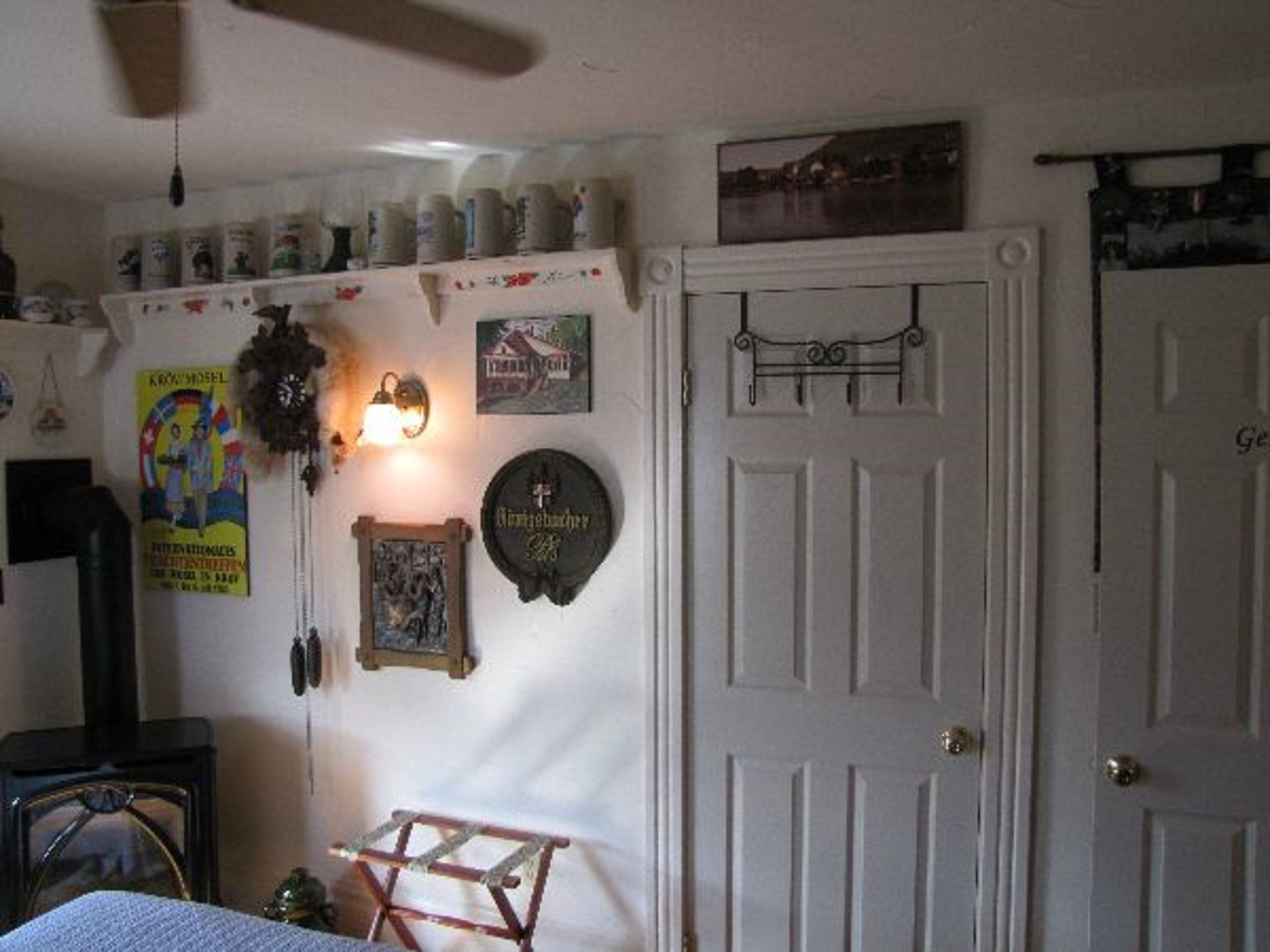 A room with a white door, a small wooden stool, a wall-mounted light, and various decorations including a clock, a framed picture, and a poster.