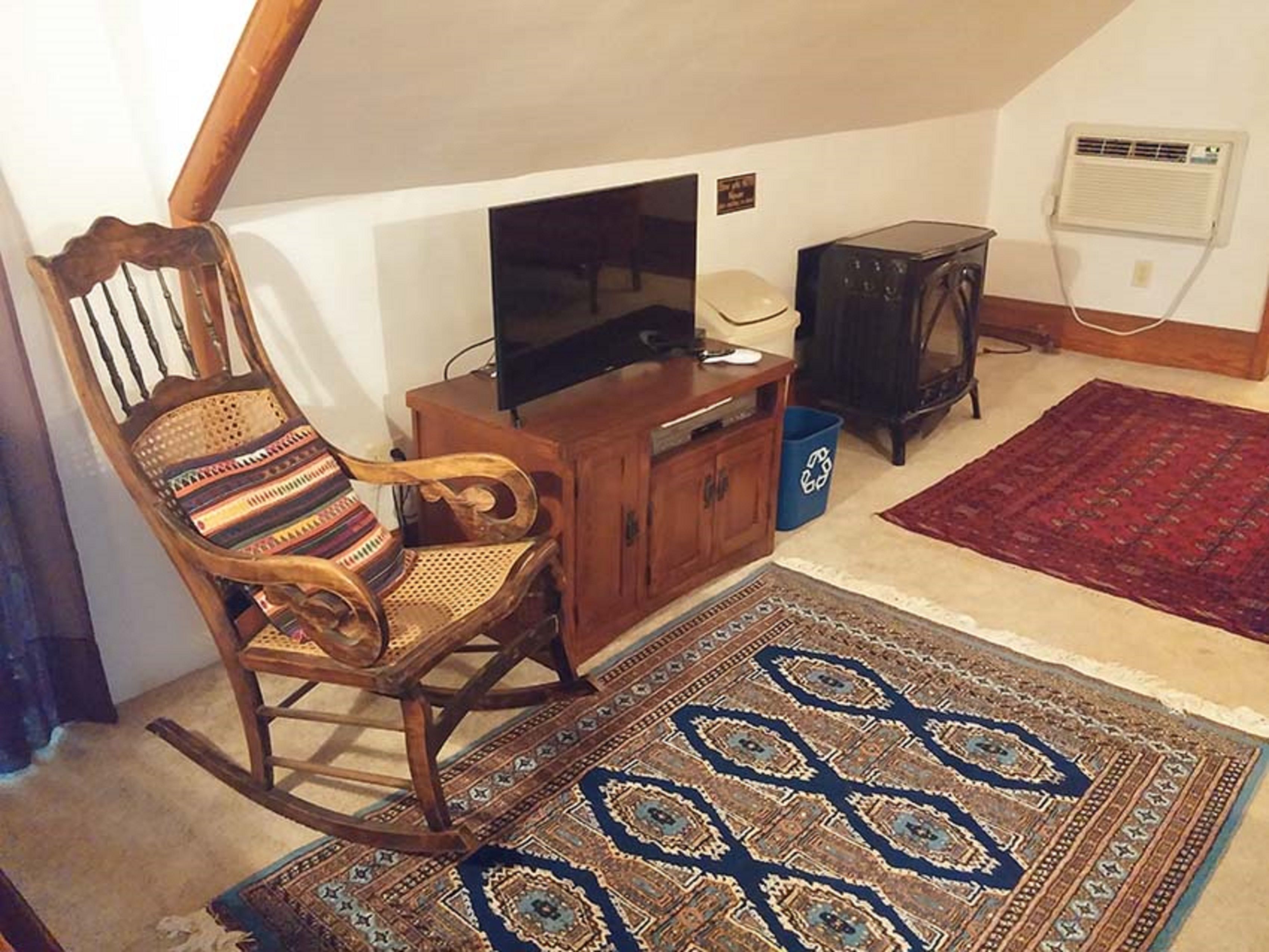 Een gezellige woonkamer met een houten schommelstoel, een televisie, een klein kastje en een kamerbreed tapijt met dessin.