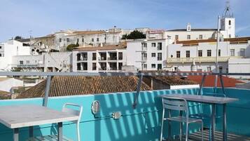 Una terraza en la azotea con mesa y sillas, con vistas a un paisaje urbano de edificios blancos y una iglesia.