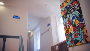 A hallway with a colorful mural, a sign reading "CARAPAU de Corridouro," and a wicker chair. - Peneco Albufeira GuestHouse - Hostel (Albufeira)