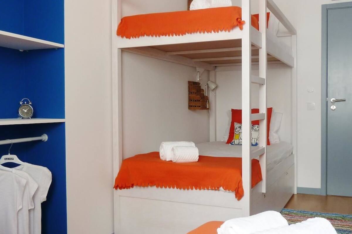 A bunk bed with orange bedding, a white wall, a blue shelf with a clock, and a door.