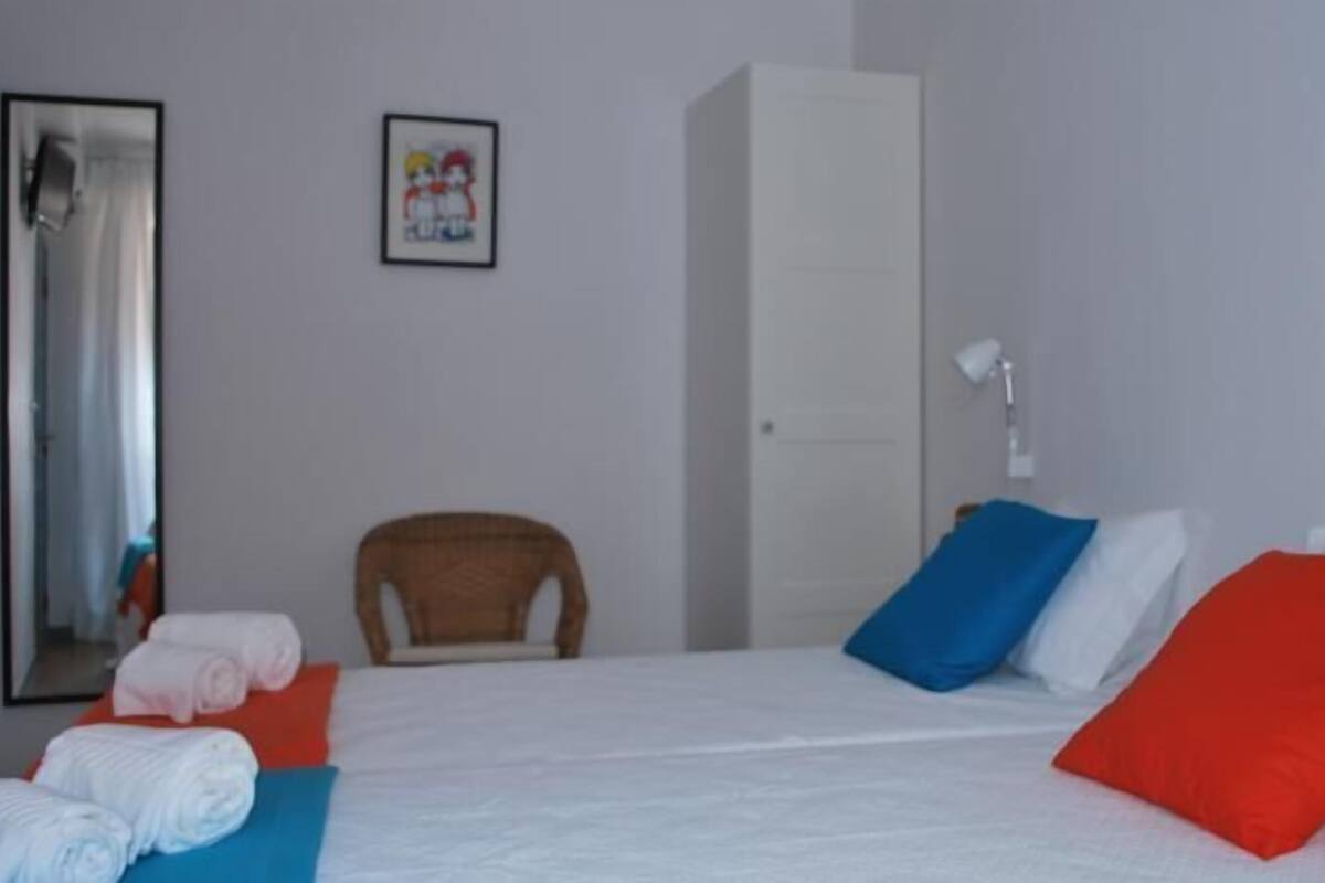 A hotel room with a bed, a chair, a wardrobe, and a framed picture on the wall.