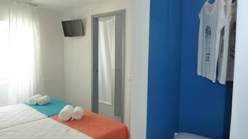 A hotel room with a bed, a TV, a shower area, and a clothing rack.