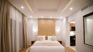 A modern bedroom with a large bed, a tufted headboard, bedside tables, and a view into the kitchen. - Arabella Residence (New Cairo)