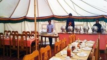 A large tent with tables set for dining, chairs, and a buffet area with food containers.