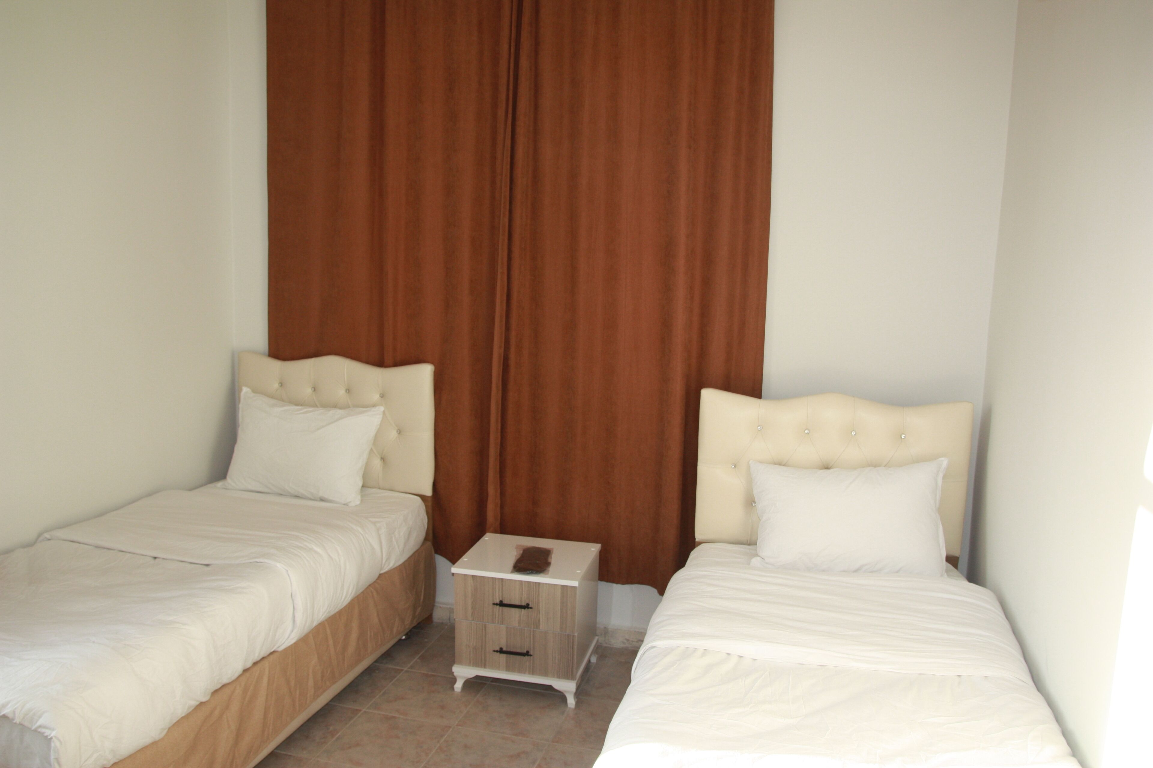 Habitación doble con dos camas, una mesita de noche de madera y una cortina marrón.
