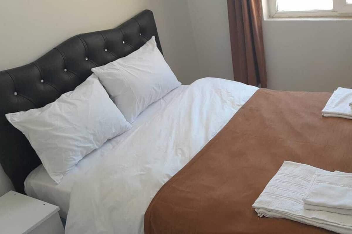 Un lit bien fait, avec du linge de lit blanc et marron, une tête de lit noire et deux serviettes blanches pliées posées sur le pied de lit.