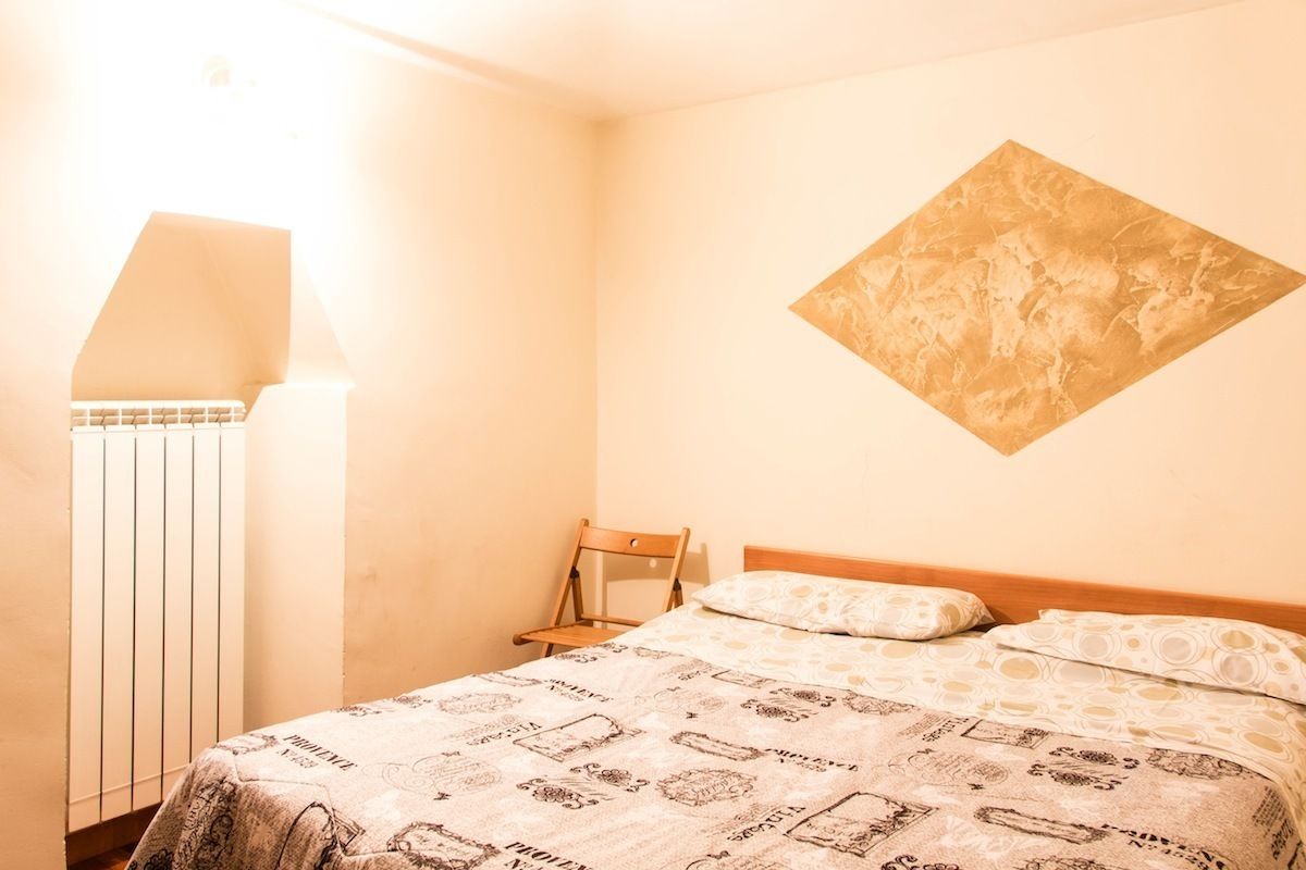 Una camera da letto con un letto, una sedia, un termosifone e un'opera d'arte appesa al muro.