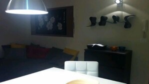 Un comedor con una mesa blanca, un bol y una taza. Hay un sofá con cojines y un cuadro en la pared.