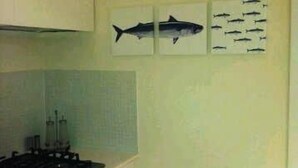 Una cocina con armarios blancos, una estufa y un lavamanos. Encima de la estufa hay tres cuadros en la pared.