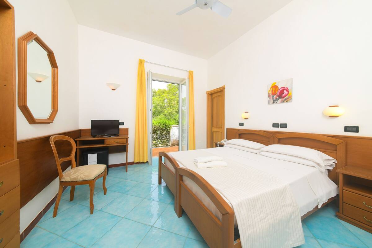 A hotel room with a bed, desk, chair, and a door leading to a balcony.
