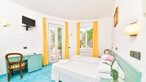 Habitación de hotel con cama, escritorio, silla, televisión y ventana con cortinas.