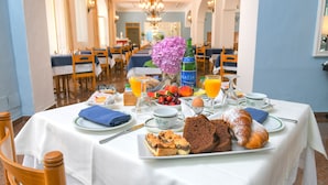 A breakfast table set with various foods, drinks, and a vase of flowers. - Hotel Pineta (Ischia)
