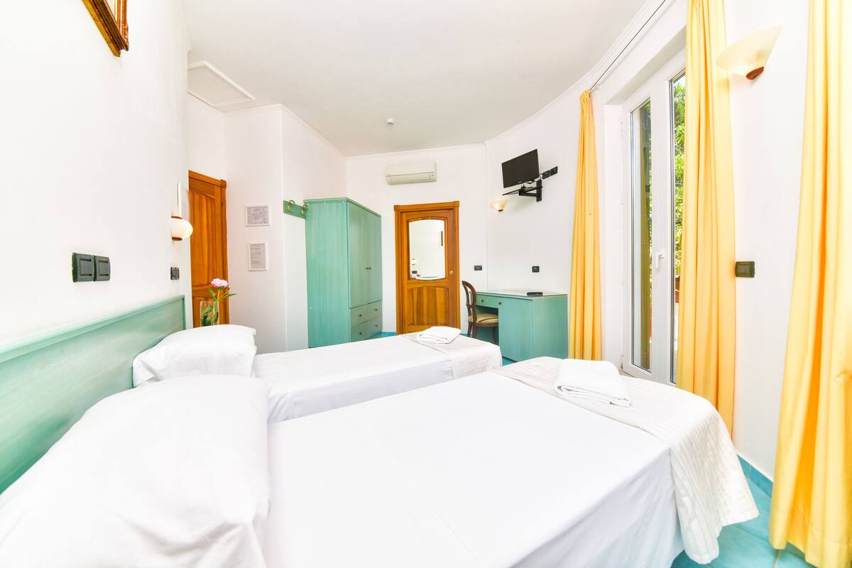 A hotel room with two single beds, a desk, a mirror, and a sliding glass door to the outside.
