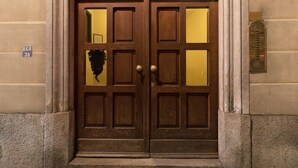 Puerta doble de madera con paneles de vidrio y un timbre de bronce.