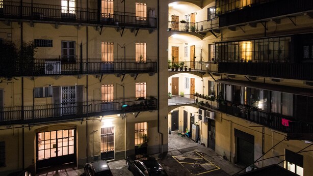 Un edificio de varios pisos con balcones, un patio interior y un automóvil estacionado en el nivel inferior.