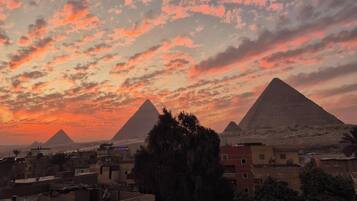 A sunset view of the pyramids with buildings in the foreground.