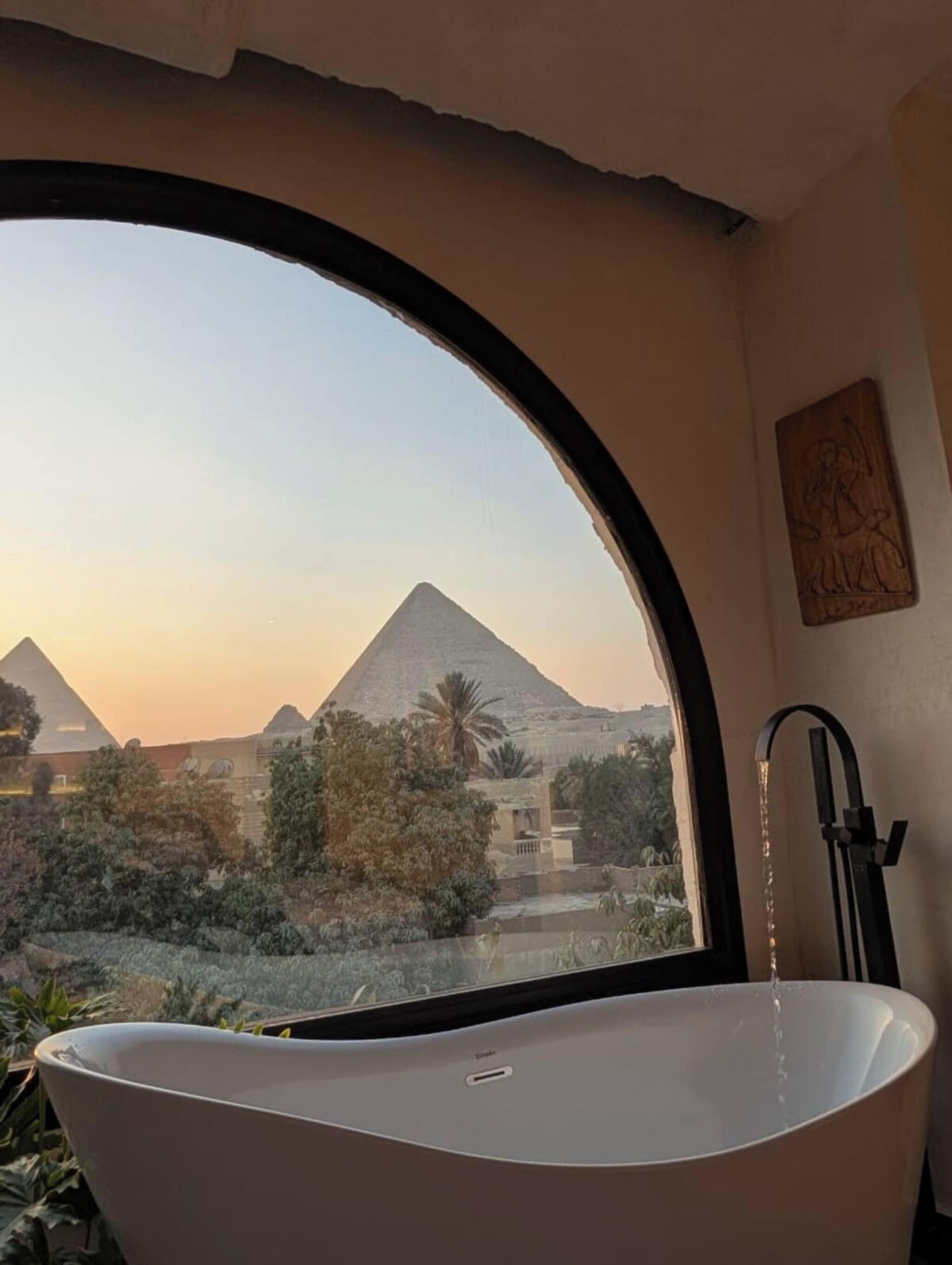 A bathtub with a view of the pyramids through a large arched window.