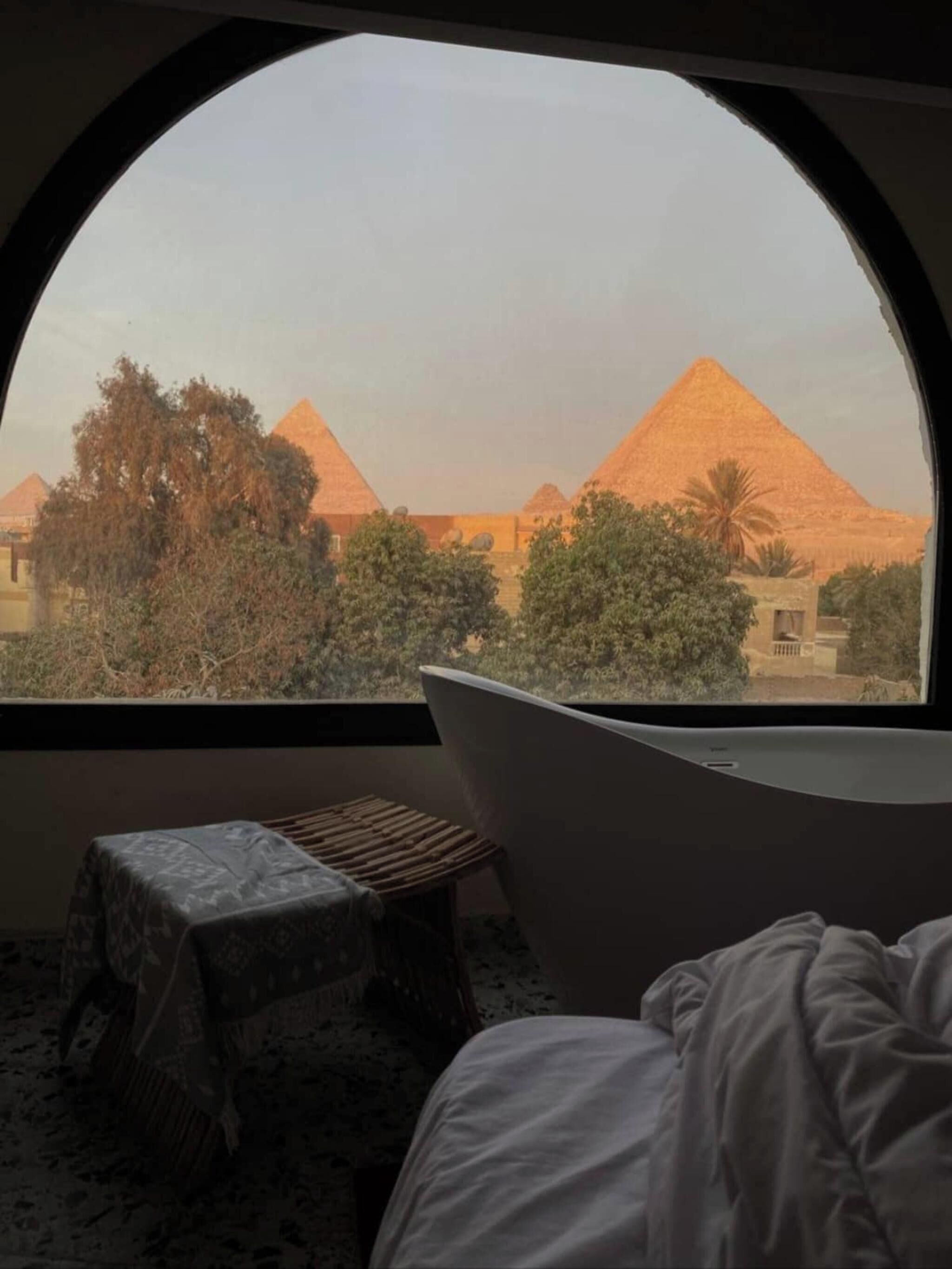A room with a view of pyramids, a bathtub, and a small stool.