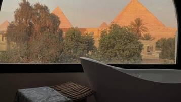 A room with a view of pyramids, a bathtub, and a small stool.