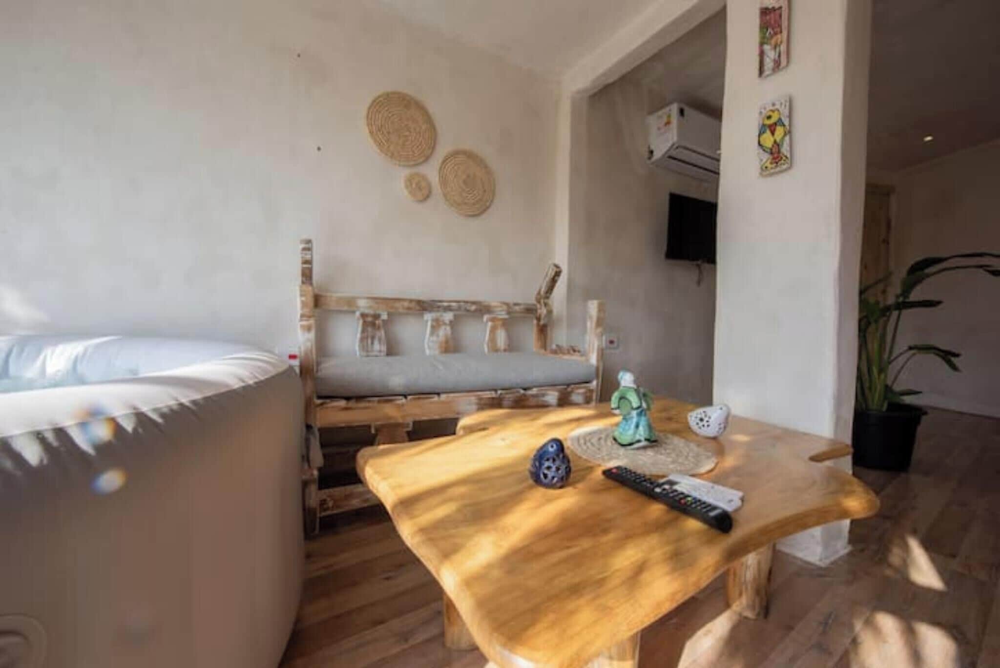 A room with a bed, a wooden table with a remote control, a small statue, and a wall-mounted air conditioner.