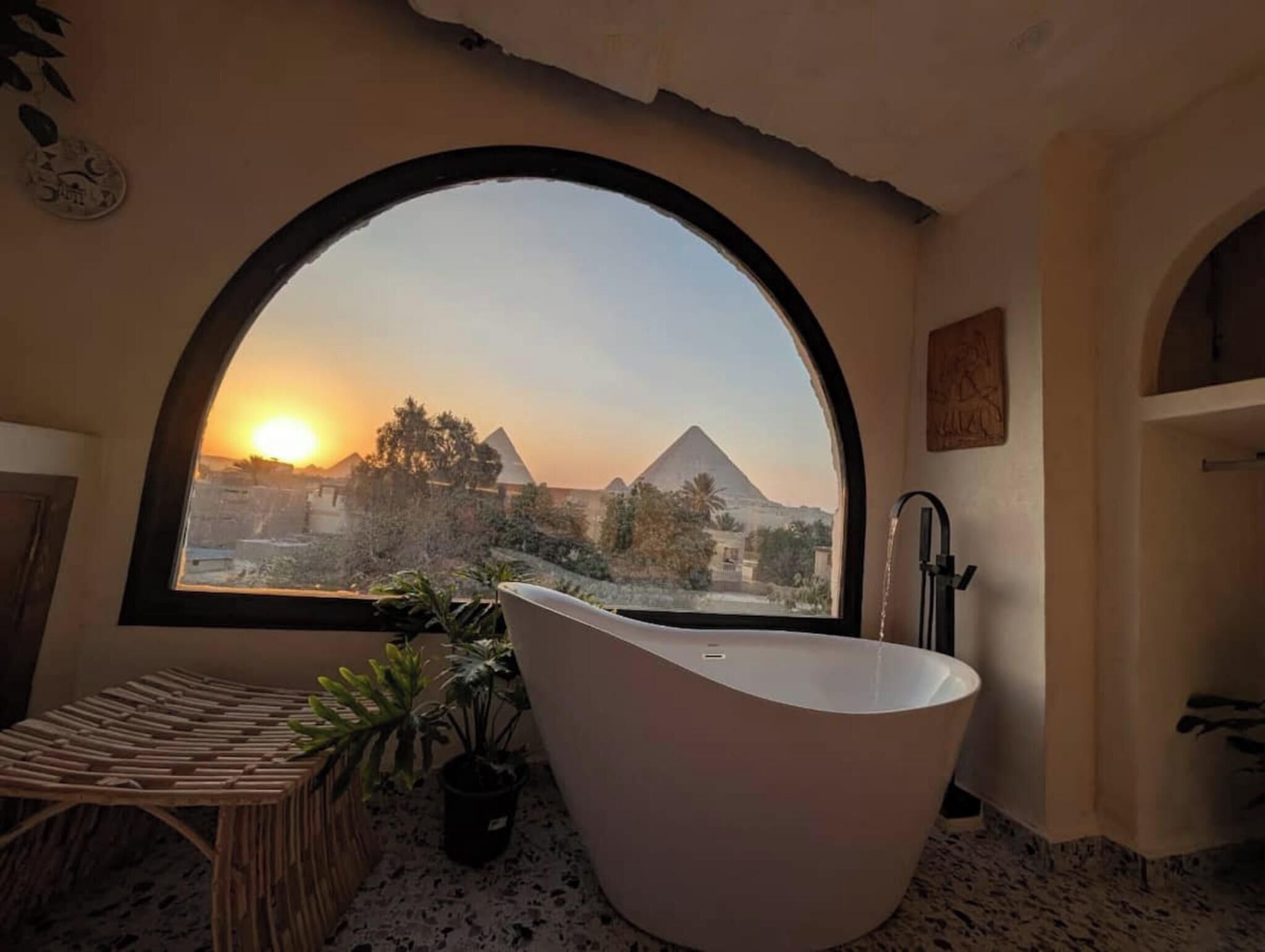 Un baño con un amplio ventanal de arco, una bañera independiente y una mesita con plantas.