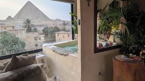 Une pièce avec vue sur les pyramides, un tabouret en bois, un miroir et un chat.