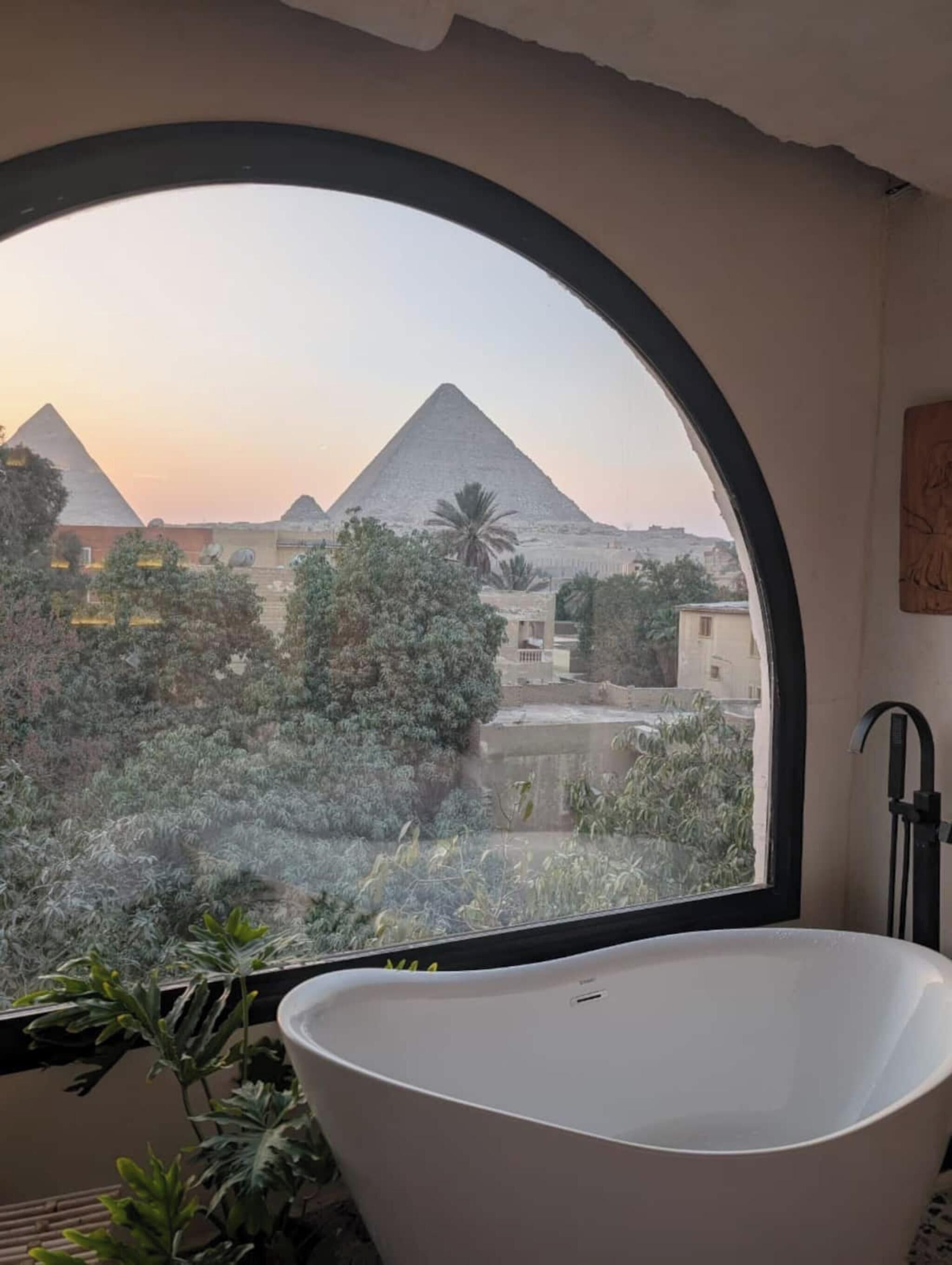 A bathtub with a view of the pyramids through a large arched window.