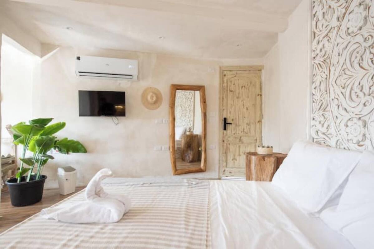 A bedroom with a bed, a potted plant, a mirror, and a television on the wall.