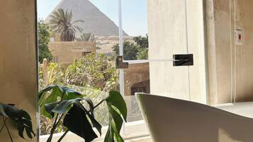 Un baño con una bañera grande, una ventana con vista a una pirámide y una planta.