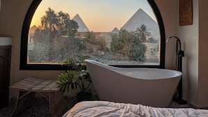 Une pièce dotée d’une grande fenêtre en arc de cercle, d’une baignoire sur pieds, d’un lit et d’une petite table agrémentée de plantes.