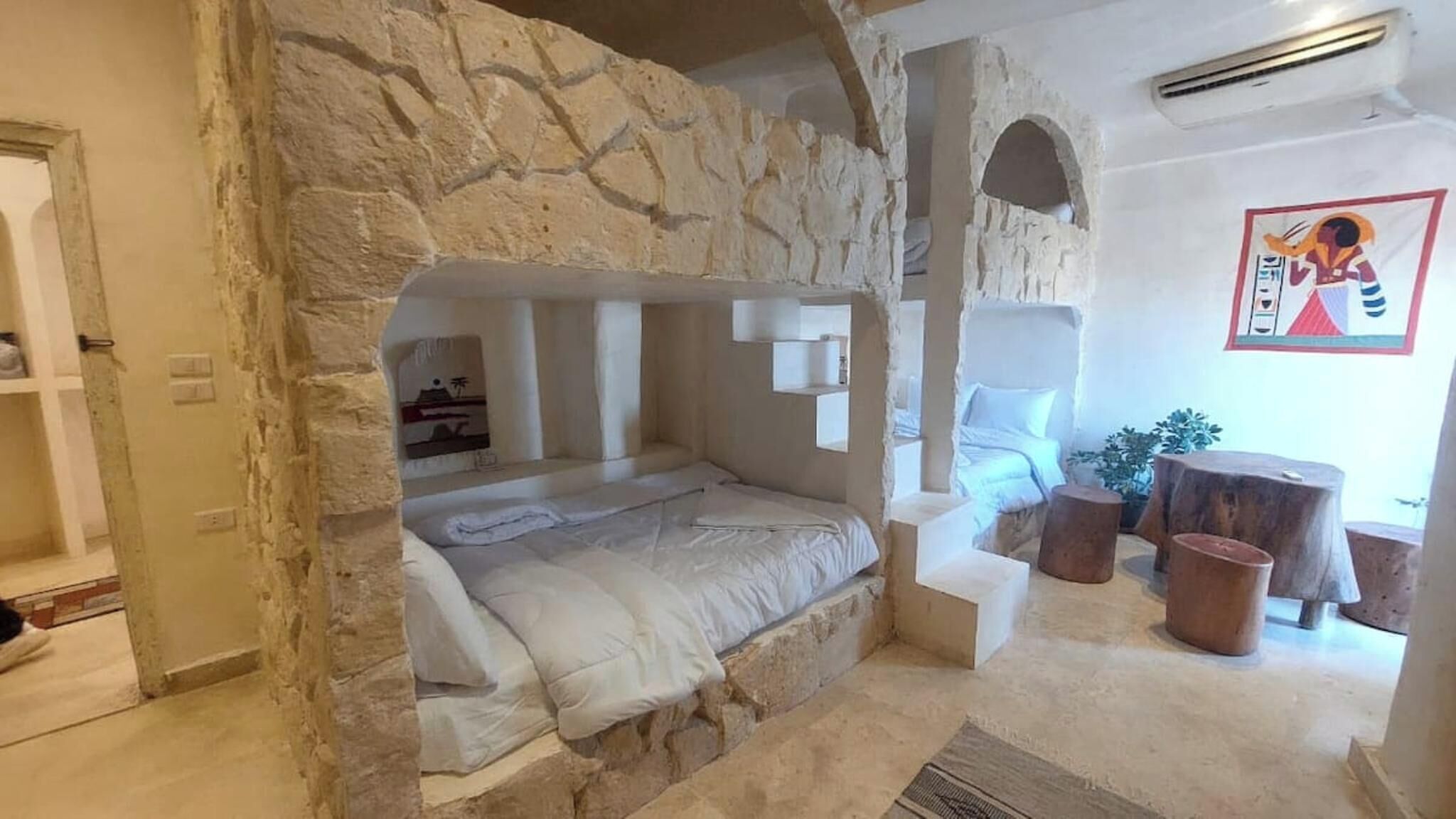 A stone-walled room with a bed, a small table, and a chair.