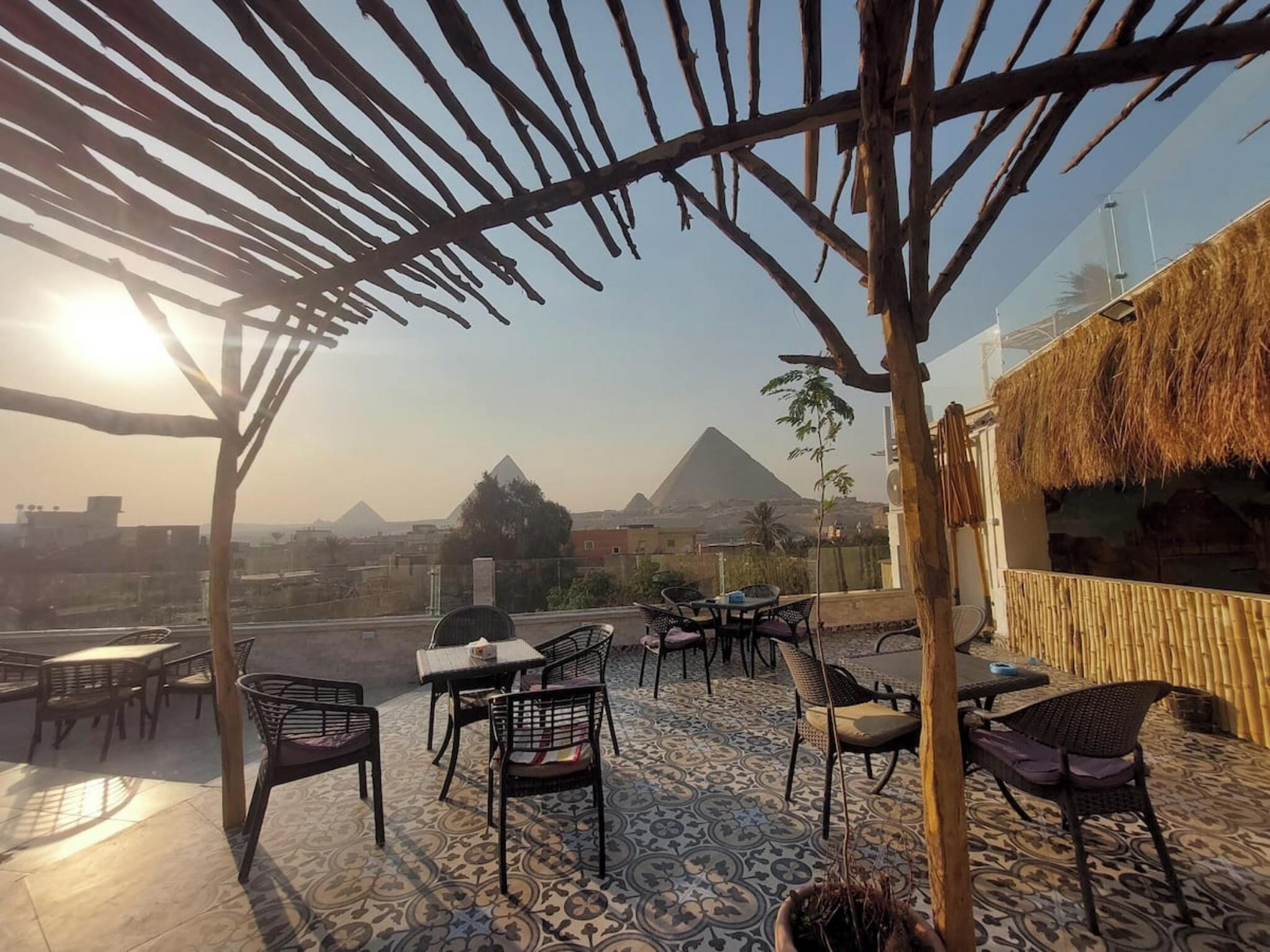 Un patio al aire libre con mesas y sillas, una pérgola y vistas a pirámides.