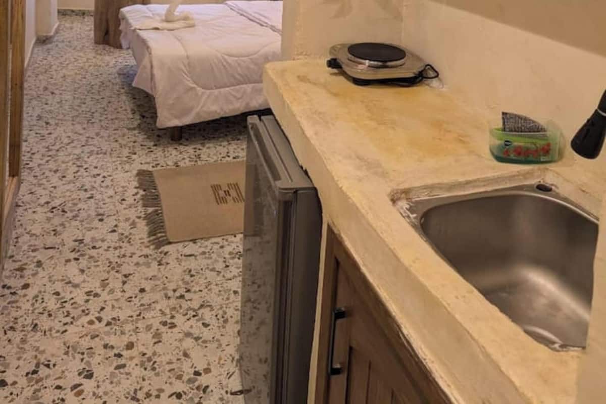 A compact hotel room with a kitchenette, a bed, a small table, and a window.