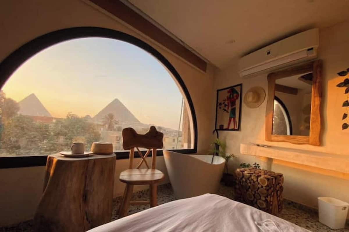 A room with a large arched window, a bed, a chair, a bathtub, and a wooden stool.