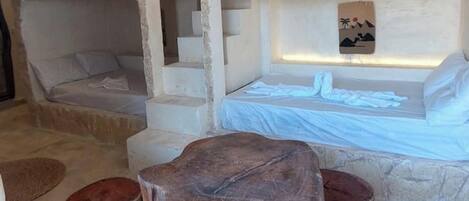 Habitación de paredes de piedra con literas, una mesa de madera y un banco de piedra.