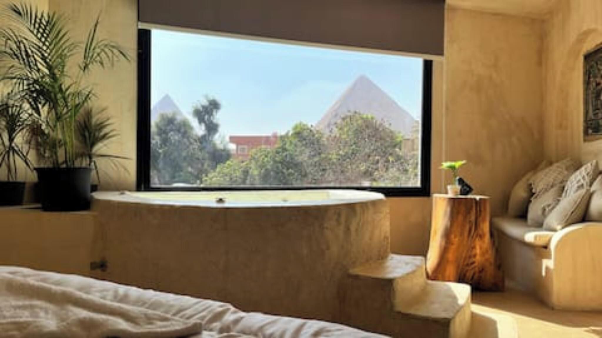 A bedroom with a large window, a bathtub, a bed, a chair, and a small table.