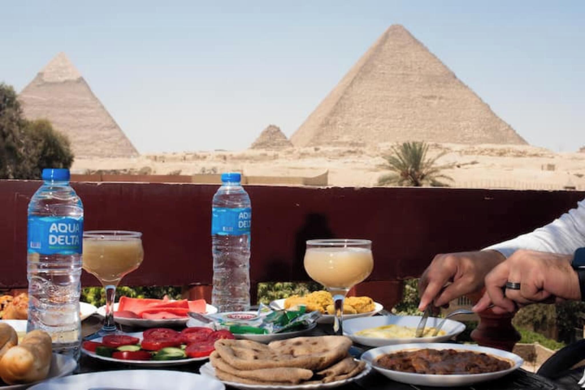 A table with food and drinks, a person eating, and pyramids in the background.