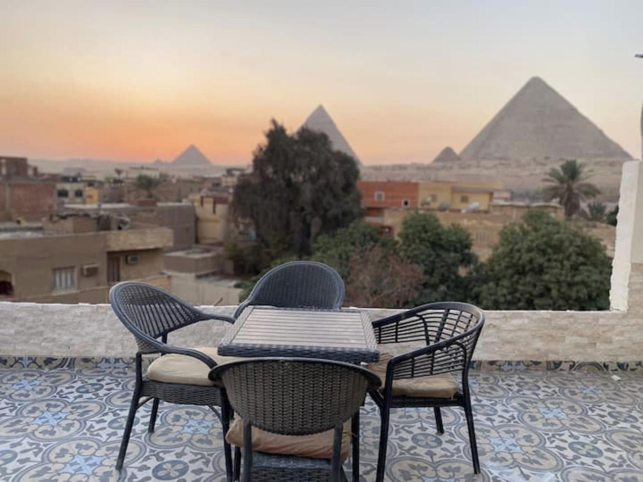 Una terraza con mesa y sillas, con vistas a un paisaje urbano donde se ven pirámides al fondo.