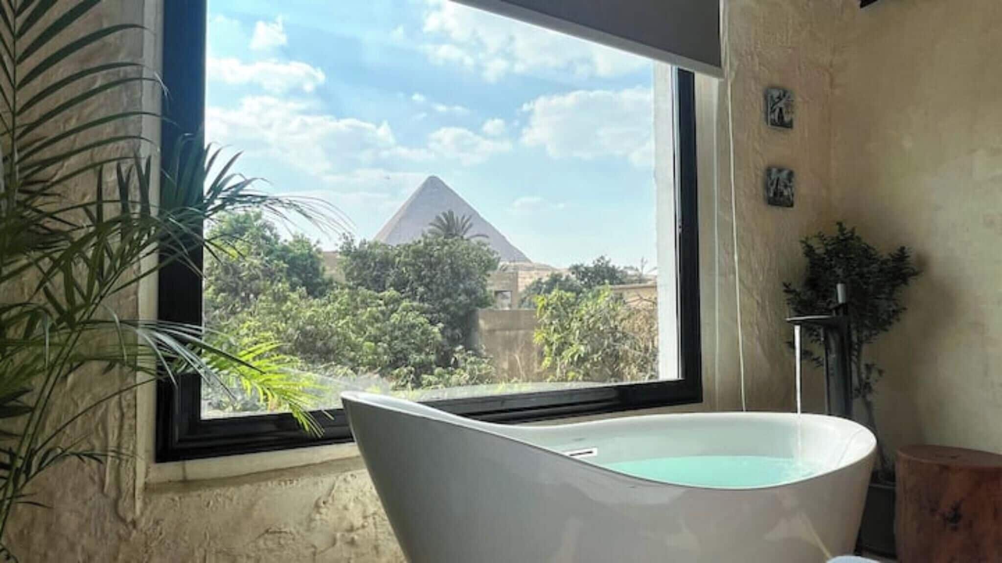 A bathroom with a bathtub, a window, and a view of a pyramid.
