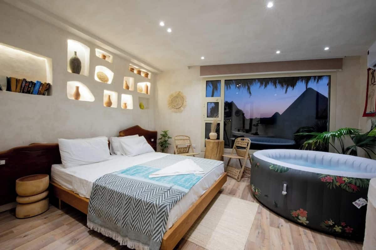 A bedroom with a bed, a small table, a chair, a hot tub, and a view of the mountains.