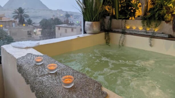 Une chambre avec vue sur une pyramide, une baignoire avec des bougies et des plantes en pot.